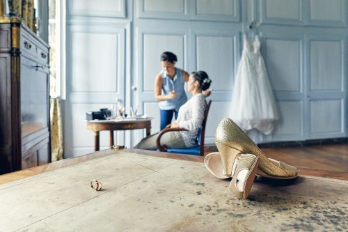 Les préparatifs de la mariée avec la robe de mariage en arrière plan et les chaussures et alliances au premier plan dans la magnifique chambre du Château de Salvanet